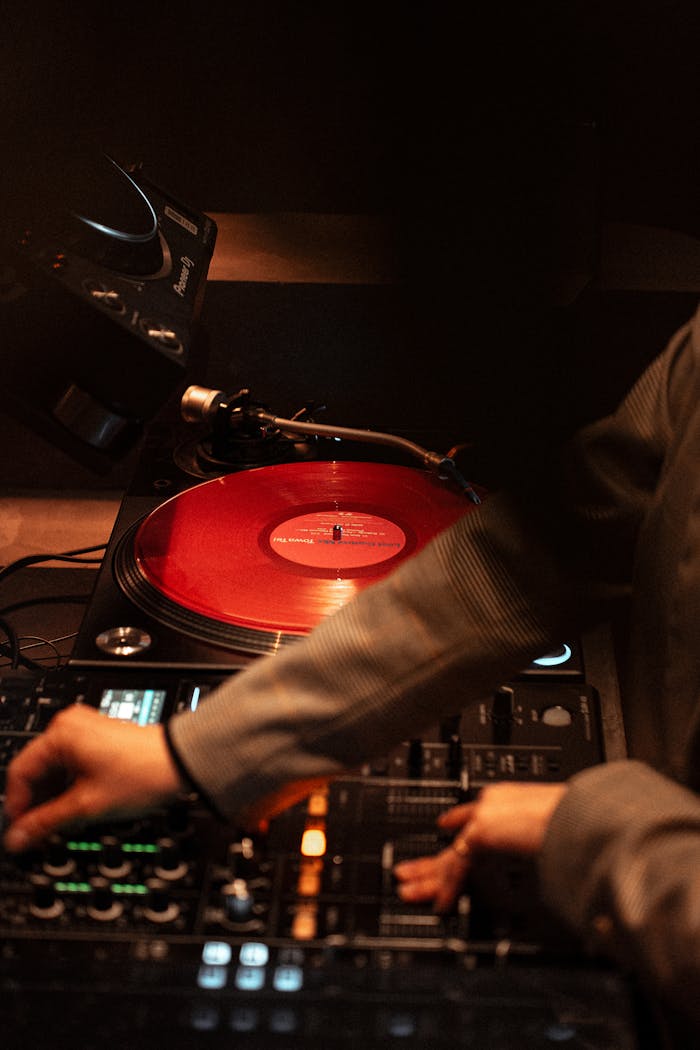 A DJ skillfully mixes music on a red vinyl in a Tokyo nightclub, creating a lively atmosphere.